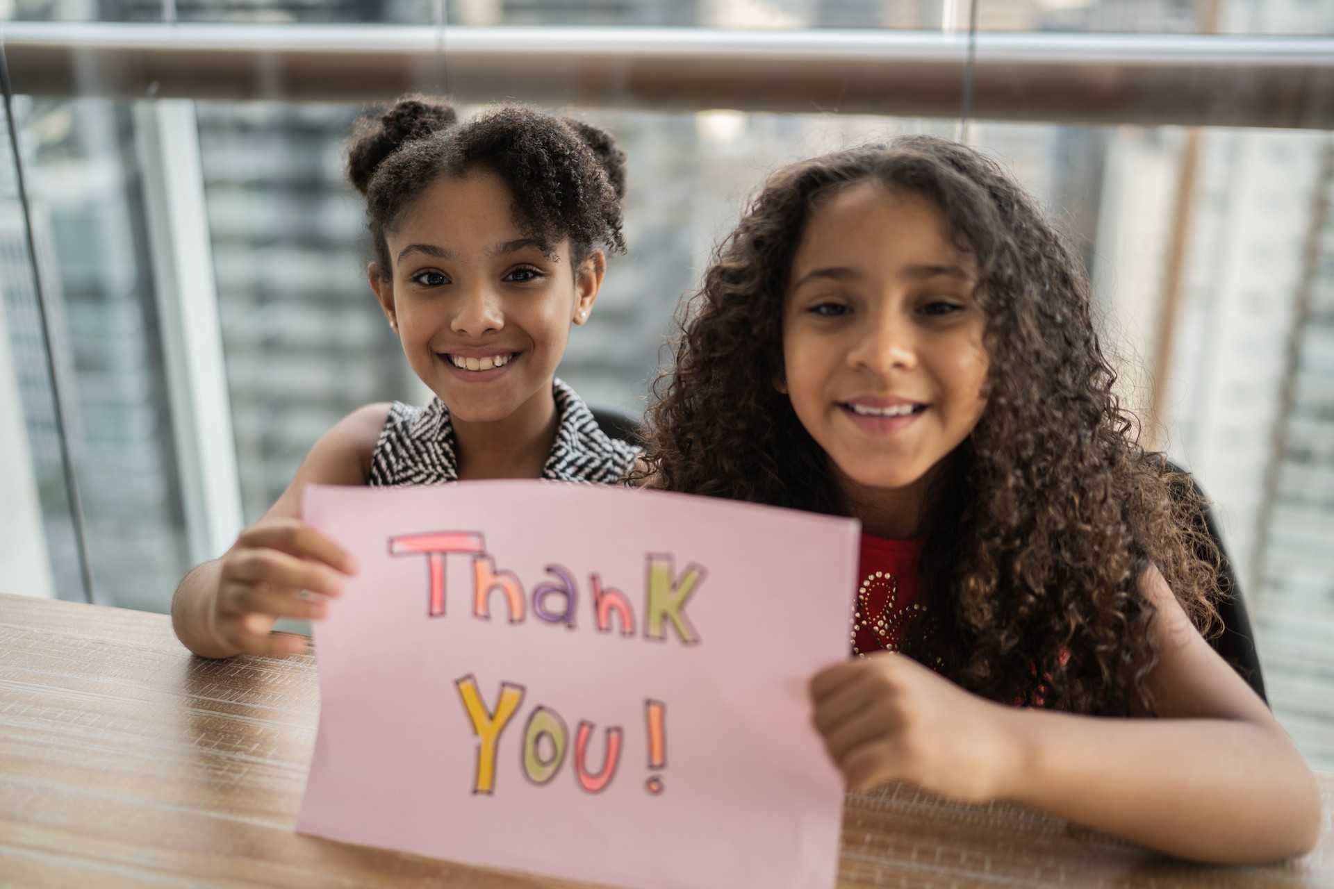 Portrait of sisters holding paper with 'thank you' written at home